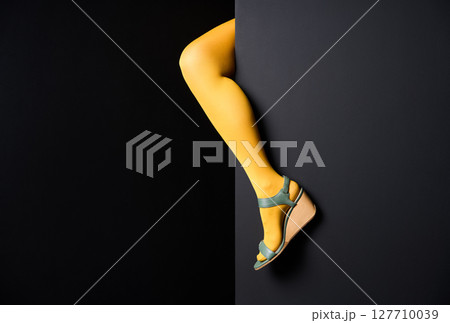 Woman leg in yellow tights emerging from black wall background. 127710039