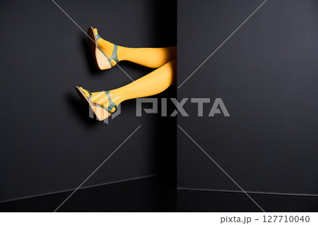 Female legs in yellow tights and elegant sandals emerging from black background Female legs in yellow tights and elegant sandals emerging from black background 127710040