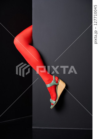 Woman leg in red tights emerging from black wall background. Woman leg in red tights emerging from black wall background. 127710045