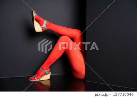 Female legs in yellow tights and elegant sandals emerging from black background Female legs in yellow tights and elegant sandals emerging from black background 127710049