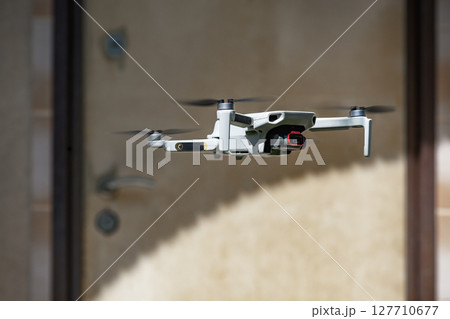 Small Flying Quadcopter Drone in flight mode with camera outdoor in front of the door of a residential building in the shade Small Flying Quadcopter Drone in flight mode with camera outdoor in front of the door of a residential building in the shade 127710677