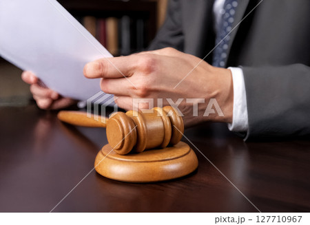 a lawyer works with documents and a wooden gavel in a courtroom or law enforcement office 127710967