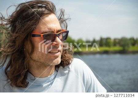 Happy caucasian brunette man in sunglasses wearing casual blue t-shirt sunglasses stand at urban park. Summer. Background for reflection. 127711034