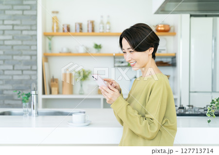 キッチンでスマホを使うミドルの女性 127713714