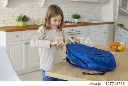 Small pupil boy packing things into blue backpack organizing items before school, learning activity 127713756