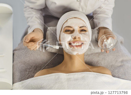 Dermatologist, cosmetologist beautician applying skin care cream mask with brush on female face 127713798