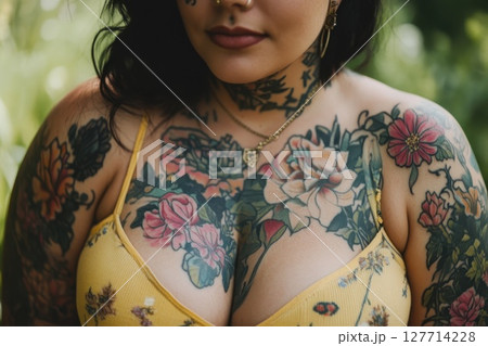 Tattooed woman in a floral top poses outdoors surrounded by greenery during a sunny afternoon in spring 127714228