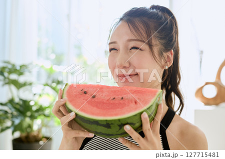 部屋でスイカを食べる若い女性の夏らしいライフスタイル 部屋でスイカを食べる若い女性の夏らしいライフスタイル 127715481