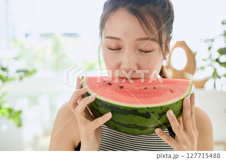 部屋でスイカを食べる若い女性の夏らしいライフスタイル 127715488