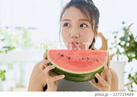 部屋でスイカを食べる若い女性の夏らしいライフスタイル 部屋でスイカを食べる若い女性の夏らしいライフスタイル 127715489