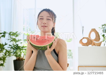 部屋でスイカを食べる若い女性の夏らしいライフスタイル 127715493