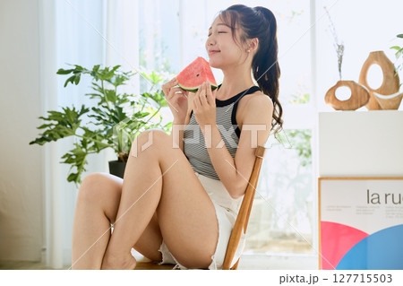 部屋でスイカを食べる若い女性の夏らしいライフスタイル 部屋でスイカを食べる若い女性の夏らしいライフスタイル 127715503