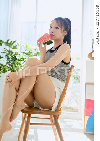 部屋でスイカを食べる若い女性の夏らしいライフスタイル 部屋でスイカを食べる若い女性の夏らしいライフスタイル 127715509