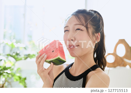 部屋でスイカを食べる若い女性の夏らしいライフスタイル 部屋でスイカを食べる若い女性の夏らしいライフスタイル 127715513