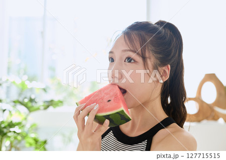 部屋でスイカを食べる若い女性の夏らしいライフスタイル 部屋でスイカを食べる若い女性の夏らしいライフスタイル 127715515