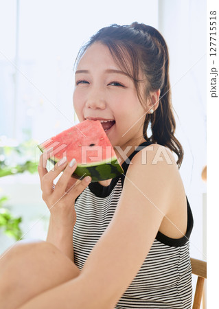 部屋でスイカを食べる若い女性の夏らしいライフスタイル 127715518