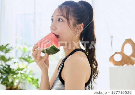 部屋でスイカを食べる若い女性の夏らしいライフスタイル 127715526