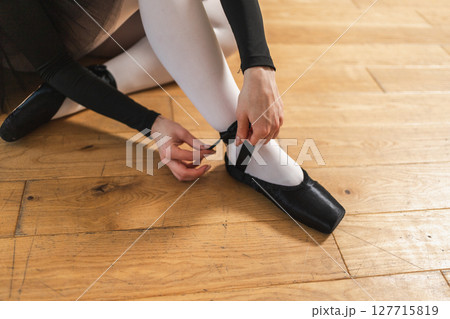 Ballerina puts on pointe shoes on leg in dance class. Classical ballet dancer woman in dance studio. Ballerina putting on tying classical pointe shoes for dance training. Ballet school concept 127715819