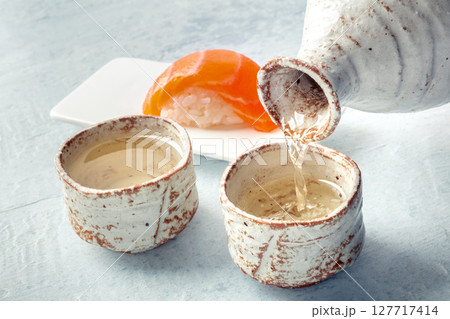 Sake poured into ochoko, traditional cup, with salmon nigiri in the background 127717414