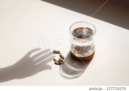 Various Capsules and Glass of Water with Hand Shadow on Light Background. Daily Vitamins and Pills for Medical Treatment. Various Capsules and Glass of Water with Hand Shadow on Light Background. Daily Vitamins and Pills for Medical Treatment. 127718278