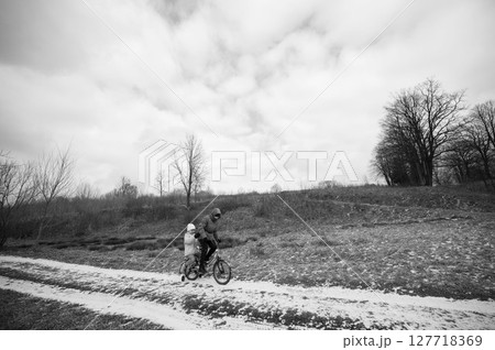 Cycling adventure through a serene landscape with a parent and child enjoying a quiet ride on a winding path surrounded by barren trees on a cloudy day 127718369