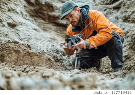 Photographer working on an archaeological dig, capturing details of soil layers in a rural outdoor setting during daylight hours 127719410
