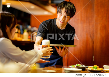 居酒屋で接客をするバイトの男性 127720076