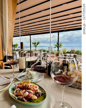 Restaurant by the sea with outdoor terrace, lunch by the sea, beautiful serving and serving with glasses and wine 127720120