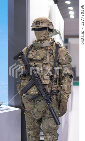 Soldier stands confidently at a military exhibition, showcasing high-tech weaponry and tactical equipment, reflecting the seriousness of modern warfare. 127720396