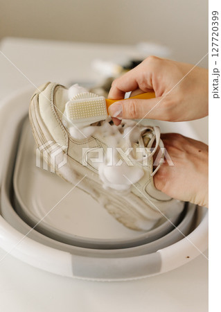 Vertical top view shot of cleaning white sneakers with small brush, removing mud stains from worn footwear in basin. Concept of hygiene, footwear free from dirt and bacteria for healthy lifestyle. Vertical top view shot of cleaning white sneakers with small brush, removing mud stains from worn footwear in basin. Concept of hygiene, footwear free from dirt and bacteria for healthy lifestyle. 127720399