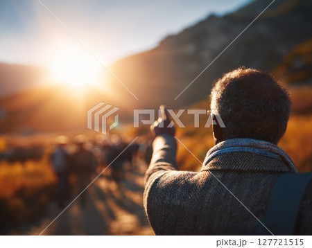 Man pointing toward horizon during outdoor retreat with group walking in warm sunlight mountain setting 127721515