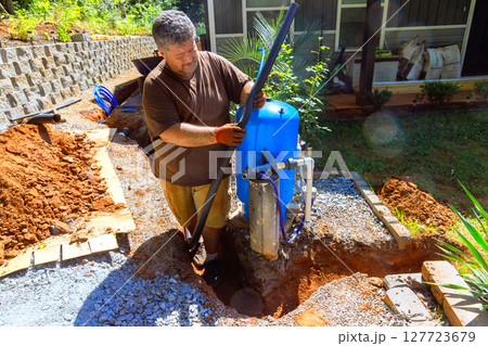 Plumber works on setting up water well pump outside, enhancing in residential area during works day 127723679