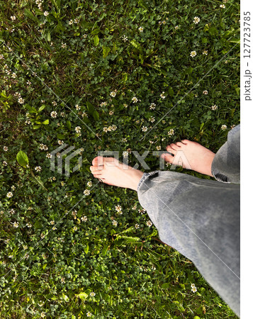 Individual is walking barefoot on vibrant green grass adorned with delicate white flowers, highlighting a serene outdoor experience and natural beauty 127723785