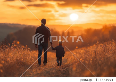 Father and son walk hand in hand during sunset in a peaceful field creating cherished moments together 127723954