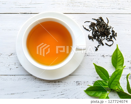 Tea in a white cup, placed on white painted wooden table, decorated with fresh and dried tea leaves. 127724074