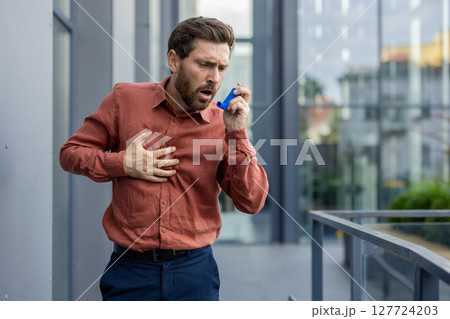 A man in an orange shirt is holding a blue inhaler. He is breathing heavily. The inhaler is blue and is in his hand A man in an orange shirt is holding a blue inhaler. He is breathing heavily. The inhaler is blue and is in his hand 127724203