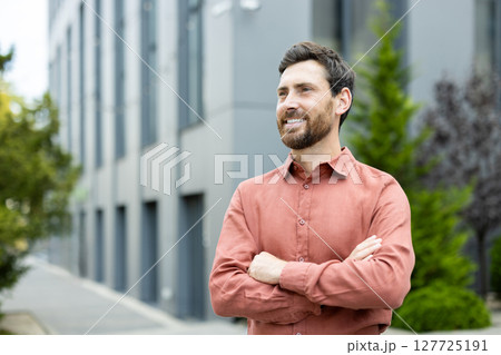 A confident, smiling man with crossed arms stands outside an office building, possibly reflecting on his success and future ventures 127725191