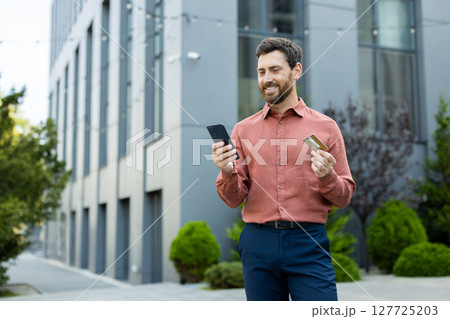 A young man in an urban environment makes use of his smartphone and credit card for seamless online shopping. 127725203