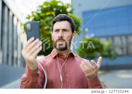 A man is actively engaged in a phone conversation outdoors while enjoying the daylight. 127725244