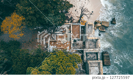 Aerial view of abandoned seaside structure amidst lush greenery and rocks Aerial view of abandoned seaside structure amidst lush greenery and rocks 127725597