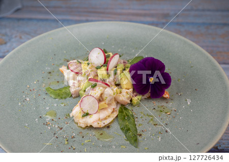 Fresh dorade and shrimp ceviche with avocado, radish, and edible flower on a decorated plate 127726434