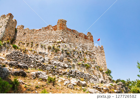 Medieval stone fortress wall with Turkish flag on top of Alanya Castle under clear blue sky 127726582