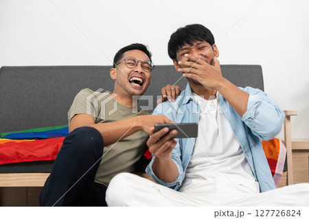 LGBTQIA Couple Sharing Laughter. Two young men enjoying a funny moment while watching something on their phone. LGBTQIA Couple Sharing Laughter. Two young men enjoying a funny moment while watching something on their phone. 127726824
