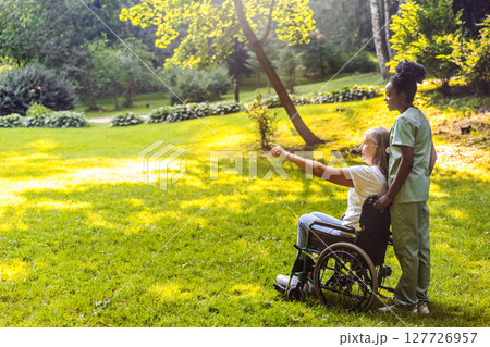 Caregiver assisting senior in rehab session in park landscape Caregiver assisting senior in rehab session in park landscape 127726957