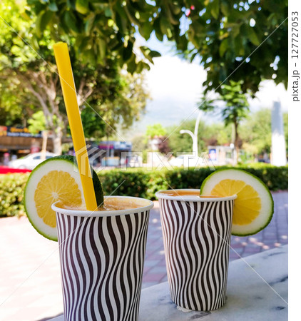 Refreshing beverages in striped cups with lemon and lime garnishes in a sunny outdoor setting Refreshing beverages in striped cups with lemon and lime garnishes in a sunny outdoor setting 127727053