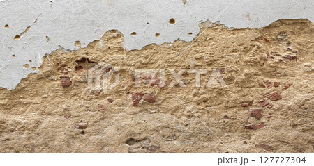 Old damaged plaster wall revealing red bricks underneath 127727304