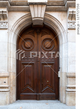 Elegant brown double door with stone arch and decorative elements Elegant brown double door with stone arch and decorative elements 127727350