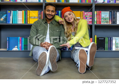Multicultural man and woman sitting on floor in library Multicultural man and woman sitting on floor in library 127727352