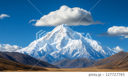 Snow capped mountain peak under fluffy cloud in bright sunlight 127727765