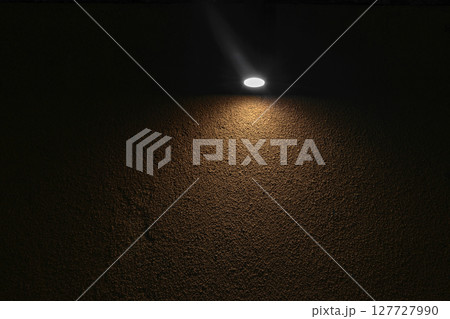 Lonely lamp illuminating brown concrete wall in absolute darkness 127727990